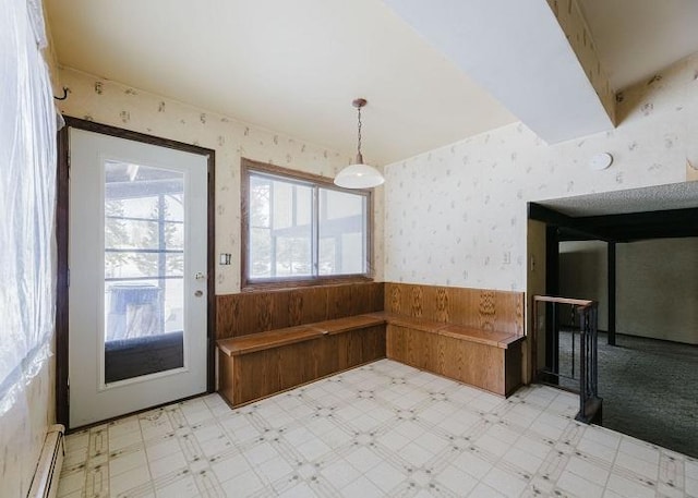 unfurnished dining area with wallpapered walls, light floors, and wainscoting