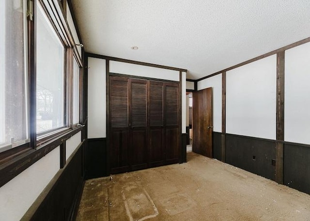 unfurnished bedroom featuring ornamental molding, a closet, wainscoting, and a textured ceiling