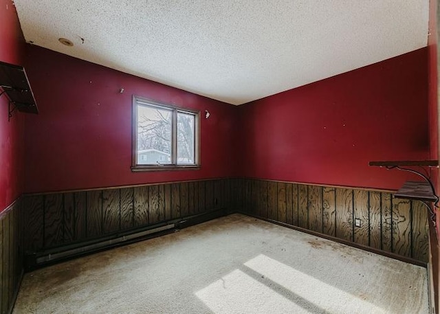 unfurnished room with a textured ceiling, a baseboard radiator, wooden walls, carpet flooring, and wainscoting