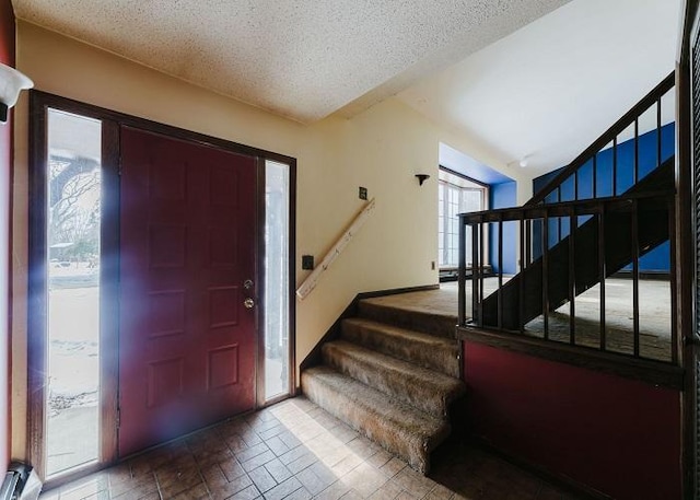 foyer featuring brick floor, stairs, vaulted ceiling, and a textured ceiling