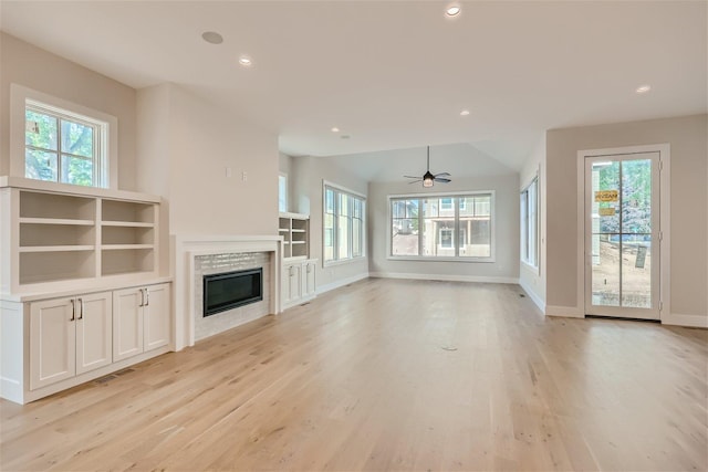 unfurnished living room featuring light wood-style flooring, a glass covered fireplace, a wealth of natural light, and recessed lighting