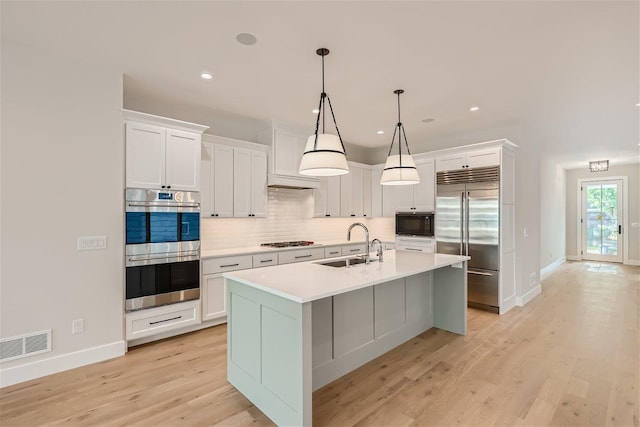 kitchen featuring light wood finished floors, visible vents, built in appliances, a sink, and backsplash