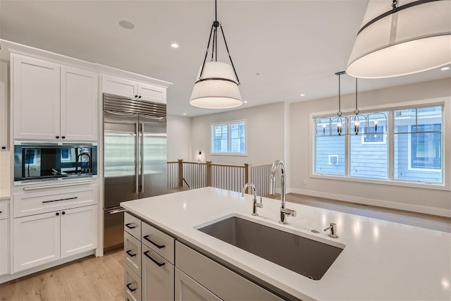 kitchen with white cabinets, built in appliances, hanging light fixtures, light countertops, and a sink