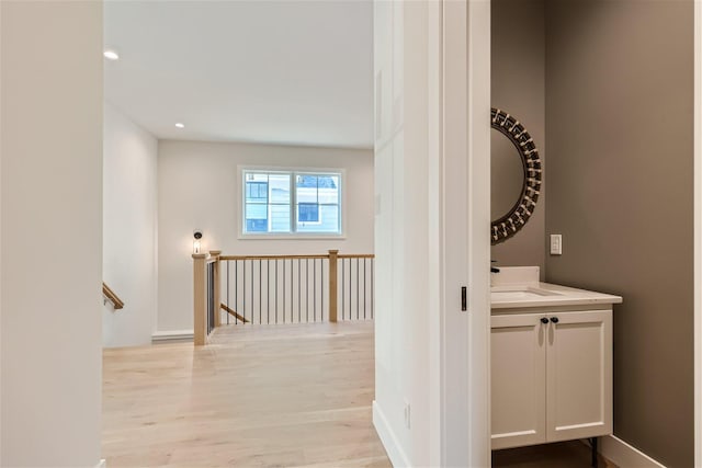hall featuring light wood finished floors, recessed lighting, a sink, and an upstairs landing