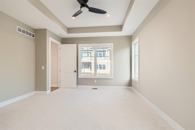 carpeted spare room featuring a tray ceiling, a ceiling fan, visible vents, and baseboards