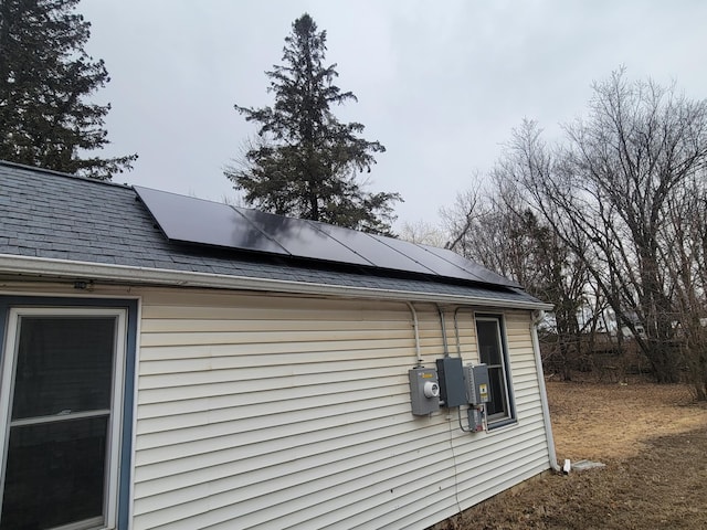 view of property exterior featuring roof mounted solar panels and roof with shingles