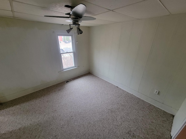 empty room featuring carpet floors, a drop ceiling, visible vents, and a ceiling fan