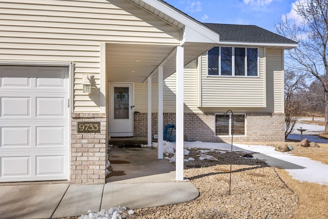 view of exterior entry with a shingled roof, brick siding, and an attached garage