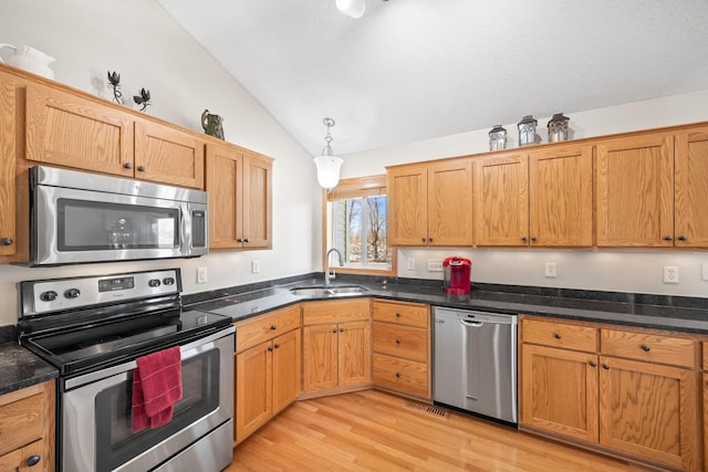 kitchen featuring stainless steel appliances, dark stone counters, vaulted ceiling, a sink, and light wood-type flooring