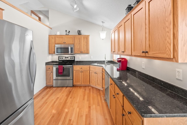 kitchen featuring a sink, light wood-style floors, vaulted ceiling, appliances with stainless steel finishes, and pendant lighting