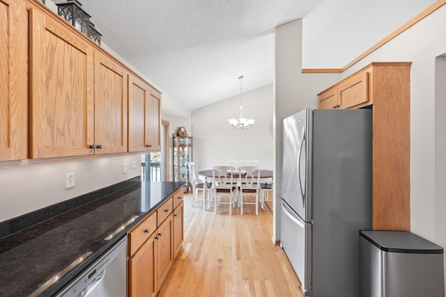 kitchen featuring lofted ceiling, light wood-style flooring, dark stone countertops, stainless steel appliances, and a textured ceiling