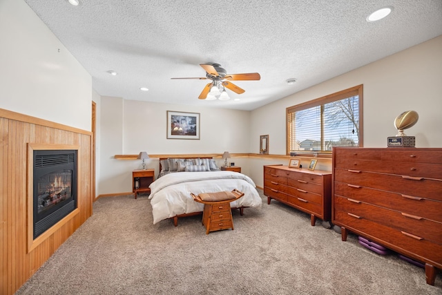 bedroom featuring carpet floors, recessed lighting, a glass covered fireplace, ceiling fan, and a textured ceiling