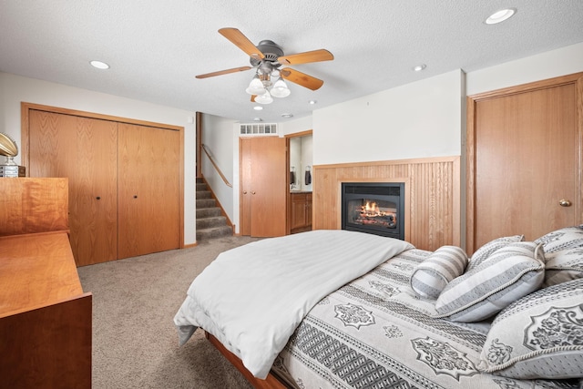 bedroom with a textured ceiling, a glass covered fireplace, carpet flooring, and visible vents