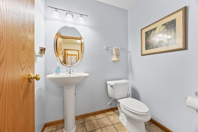 half bath with toilet, baseboards, and a sink