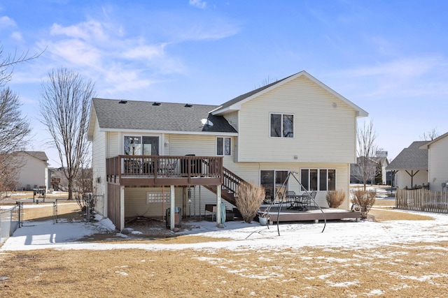 snow covered house with a shingled roof, stairway, a gate, fence, and a wooden deck