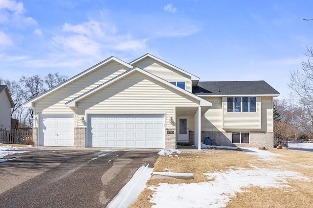 tri-level home featuring brick siding, roof with shingles, fence, a garage, and driveway