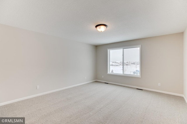 empty room with light colored carpet, visible vents, a textured ceiling, and baseboards