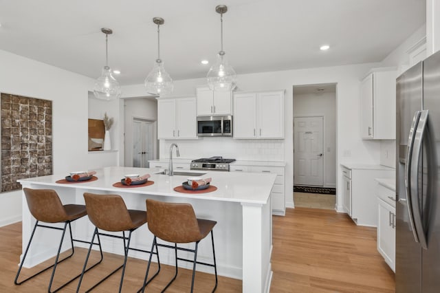 kitchen with a sink, light countertops, appliances with stainless steel finishes, backsplash, and light wood finished floors