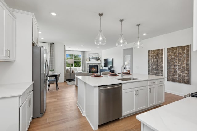 kitchen with a kitchen island with sink, light countertops, stainless steel appliances, a stone fireplace, and a sink