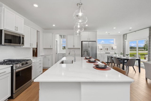 kitchen featuring an island with sink, light wood finished floors, stainless steel appliances, and a sink