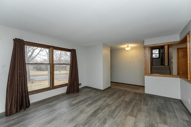 empty room with a textured ceiling, wood finished floors, and baseboards