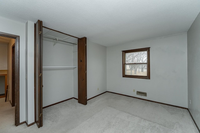 unfurnished bedroom featuring a closet, light colored carpet, a textured ceiling, and baseboards