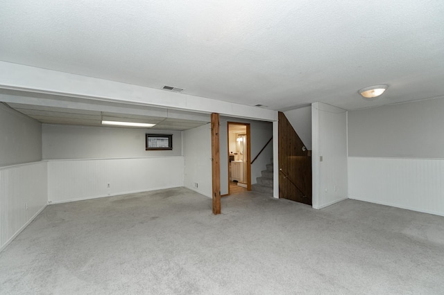 finished basement featuring visible vents, a wainscoted wall, stairway, carpet flooring, and a textured ceiling