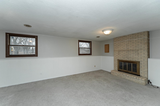 unfurnished living room with a brick fireplace, a textured ceiling, carpet flooring, and wainscoting