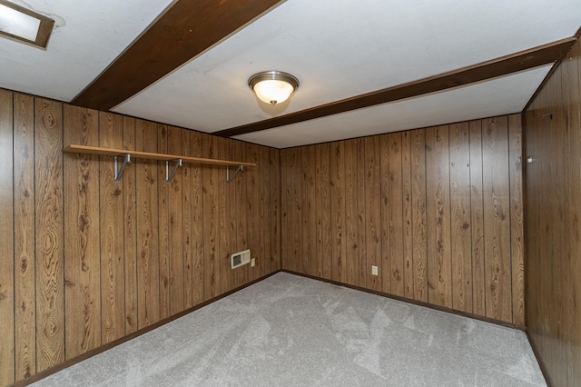 empty room featuring light carpet, wooden walls, visible vents, and beam ceiling