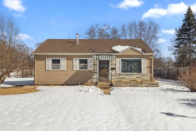 view of front of house with stone siding, a shingled roof, and fence