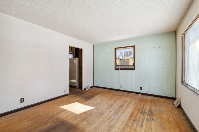 spare room with hardwood / wood-style flooring, cooling unit, baseboards, and a textured ceiling