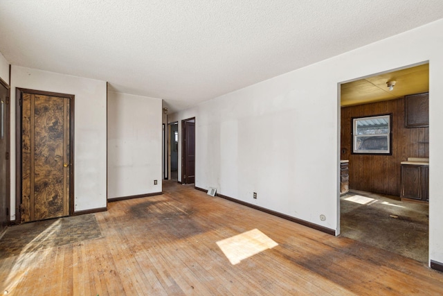 interior space with baseboards, a textured ceiling, hardwood / wood-style floors, and wooden walls