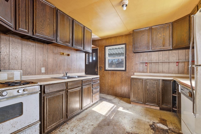 kitchen with white gas range, wood walls, light countertops, and a sink