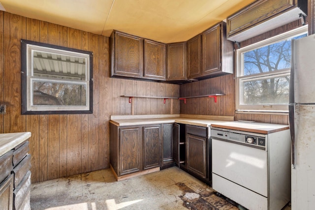 kitchen with dark brown cabinetry, wood walls, white appliances, and light countertops