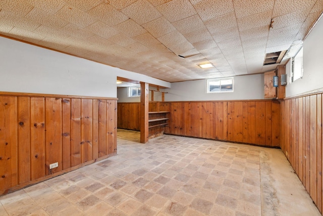 below grade area featuring a drop ceiling, a wainscoted wall, and wooden walls