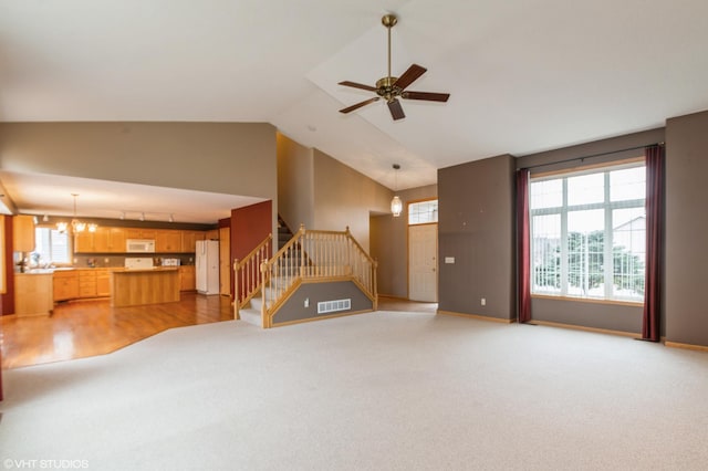 unfurnished living room featuring ceiling fan with notable chandelier, visible vents, baseboards, vaulted ceiling, and stairway