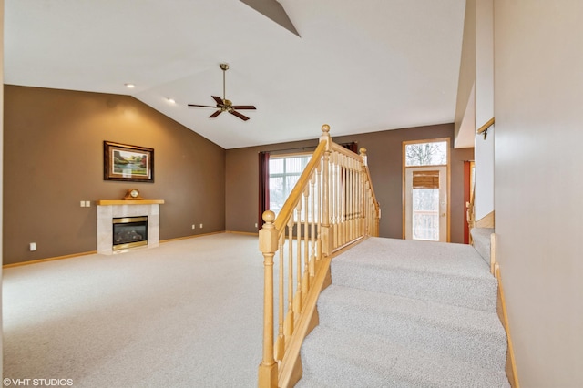 staircase with a fireplace, a ceiling fan, baseboards, vaulted ceiling, and carpet