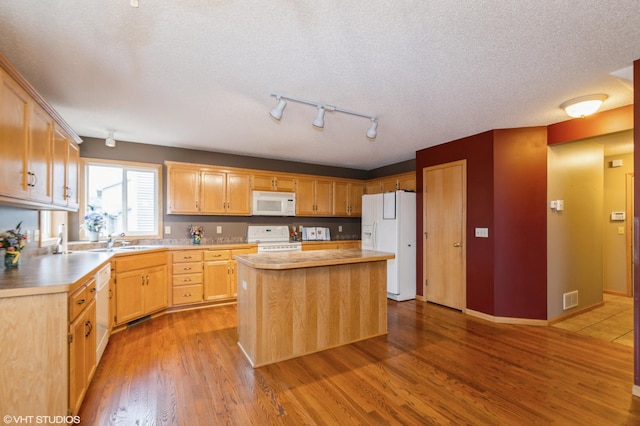 kitchen featuring white appliances, a kitchen island, a sink, visible vents, and dark wood-style floors