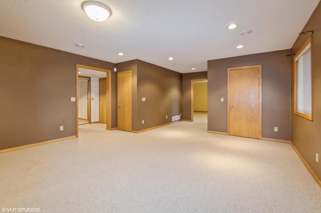 empty room with recessed lighting, light colored carpet, a textured ceiling, and baseboards