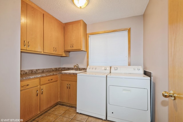 washroom with cabinet space, light tile patterned floors, washing machine and clothes dryer, a textured ceiling, and a sink