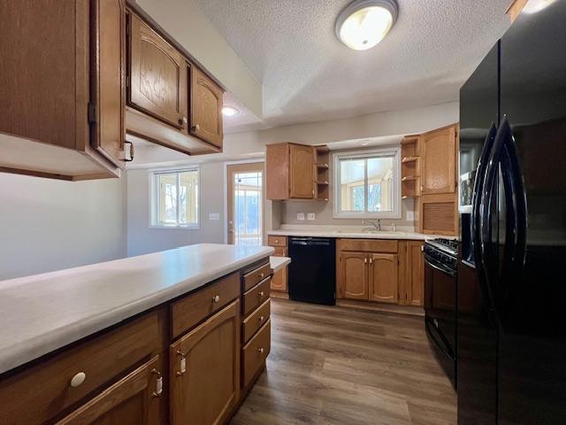 kitchen featuring wood finished floors, light countertops, a textured ceiling, black appliances, and open shelves