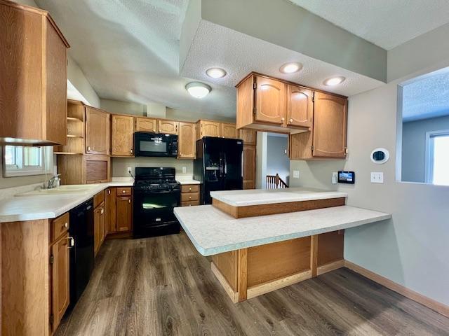 kitchen featuring dark wood-style flooring, a peninsula, black appliances, open shelves, and a sink