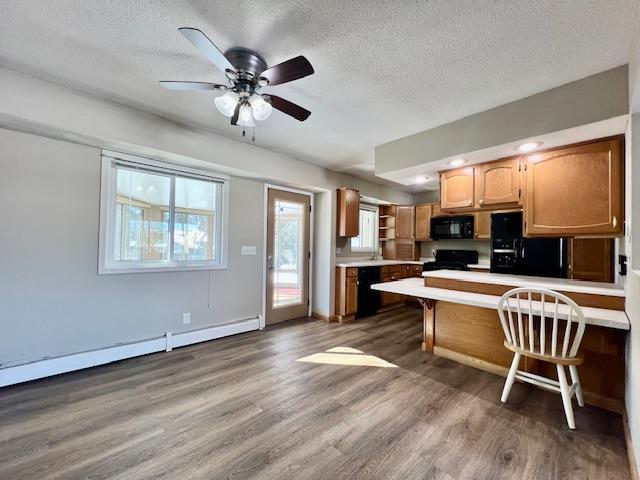 kitchen with light countertops, a textured ceiling, wood finished floors, a peninsula, and black appliances