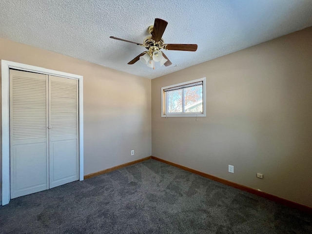 unfurnished bedroom with a textured ceiling, dark colored carpet, a closet, and baseboards