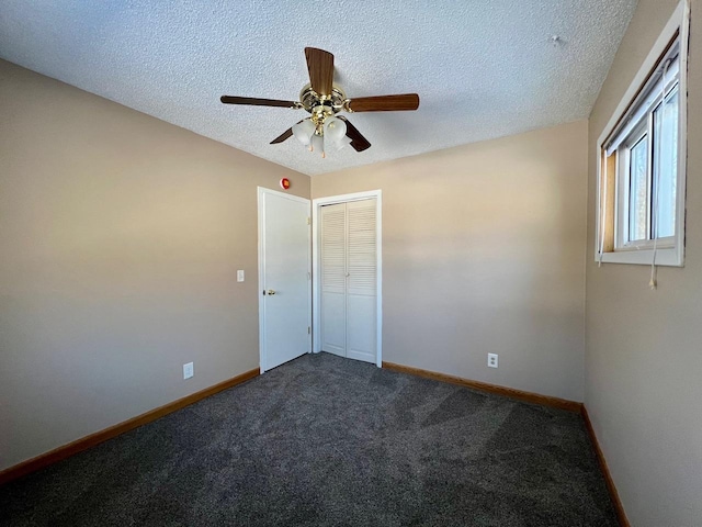 unfurnished room featuring a ceiling fan, baseboards, dark colored carpet, and a textured ceiling