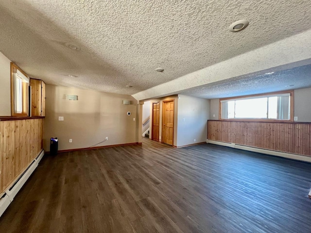 interior space with dark wood-style floors, a baseboard radiator, wooden walls, and stairs