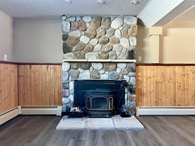 room details with a wood stove, a baseboard radiator, wood finished floors, and wainscoting