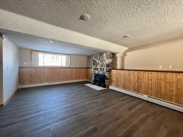 below grade area featuring a baseboard heating unit, dark wood-style flooring, wainscoting, and a textured ceiling