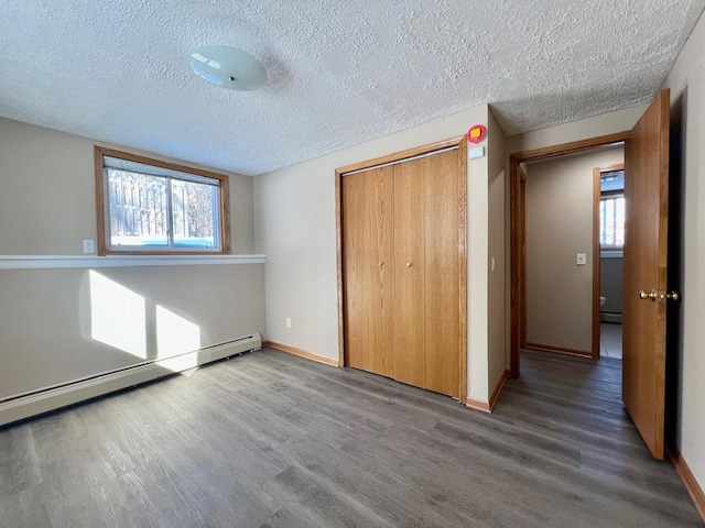 unfurnished bedroom featuring a closet, baseboard heating, wood finished floors, and baseboards