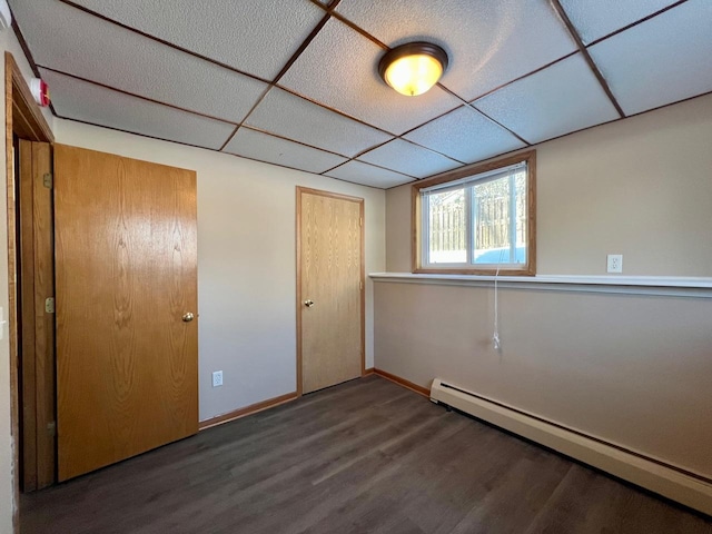 unfurnished bedroom with a drop ceiling, a baseboard radiator, wood finished floors, and baseboards